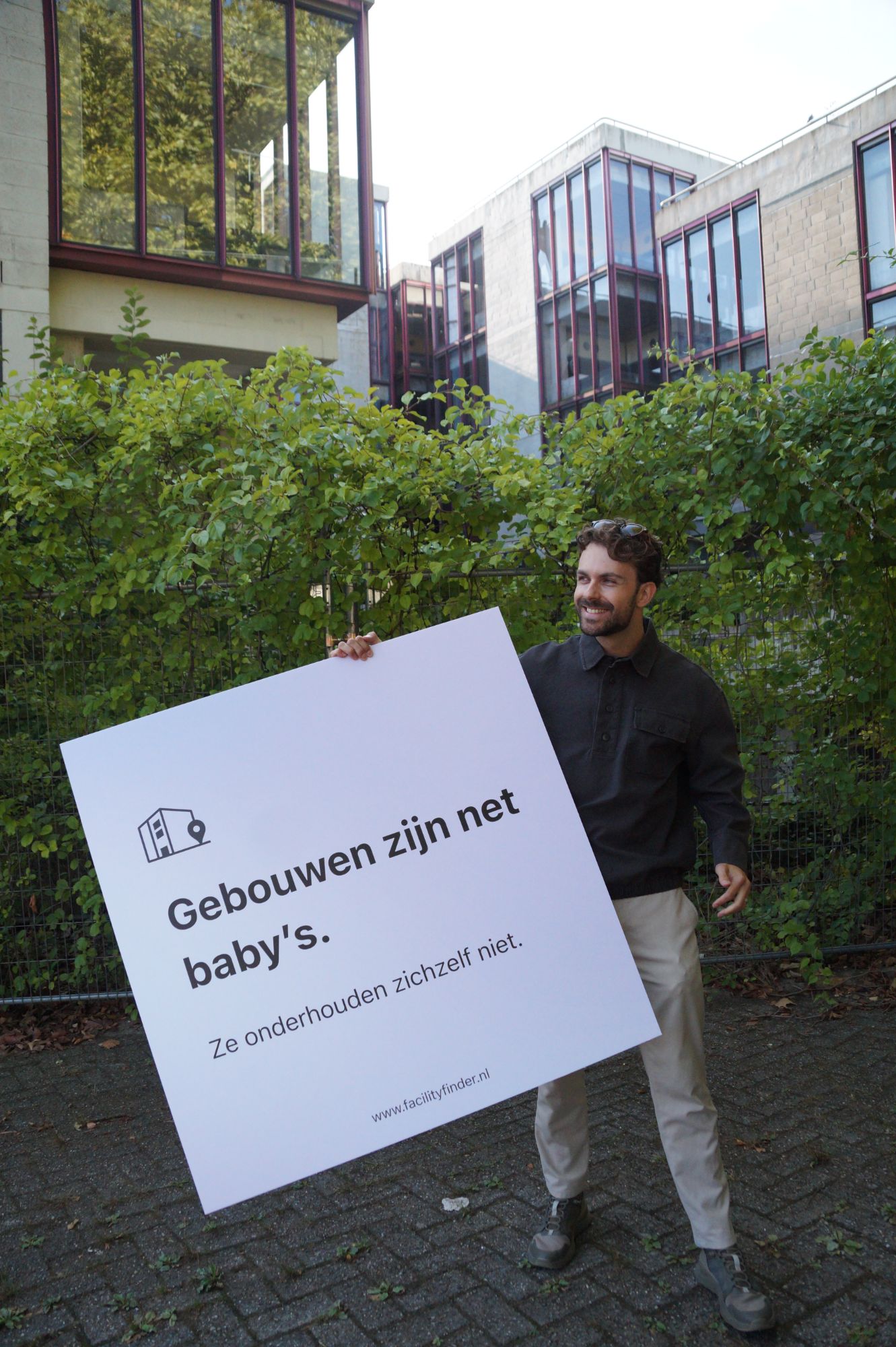 Steijn voor een kantoorgebouw met een bord: Gebouwen zijn net baby's. Ze onderhouden zichzelf niet.